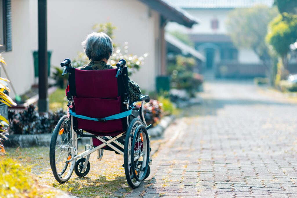 Eine ältere Person sitzt in einem Rollstuhl und sieht einsam und hilflos aus. Sie benötigt Pflege